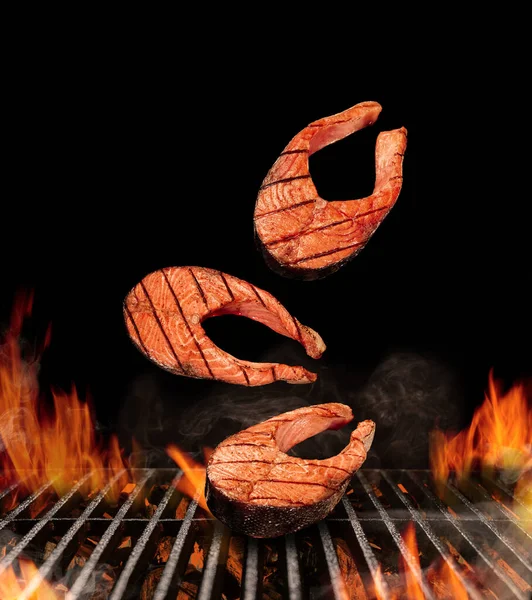 Grilled delicious salmon steaks are falling down on black background. Barbecue bbq grill, flaming fire, ember charcoal and smoke. Seafood. Close up — Stock Photo, Image