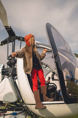 Pilot şapkalı genç kız helikopter kokpitinden uzaklığa bakıyor.