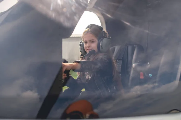 View through glass of tween girl in helicopter cockpit reaching out to dashboard — Stock Photo, Image