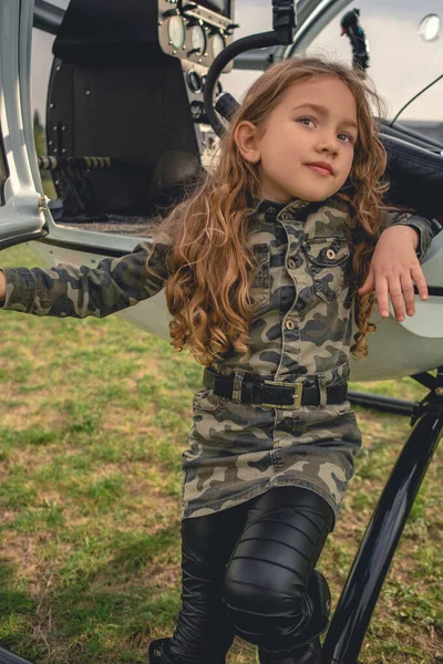 Preteen fille en robe de style camouflage debout appuyé sur hélicoptère — Photo