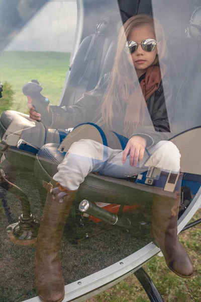 Preteen girl on pilot seat holding control handle behind glass of helicopter cockpit — Stockfoto