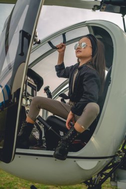 Aynalı güneş gözlüklü gülümseyen genç kız helikopter kokpitinden gökyüzüne bakıyor.