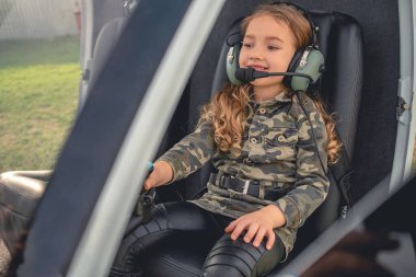Helikopterde pilot koltuğunda oturan kulaklıklı neşeli ergen kız.