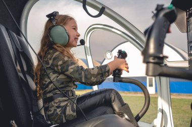 Helikopter kokpitinde oturan havacı kulaklıklı, gülümseyen genç kız.