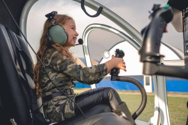 Smiling tween girl in aviator headset sitting in helicopter cockpit clipart