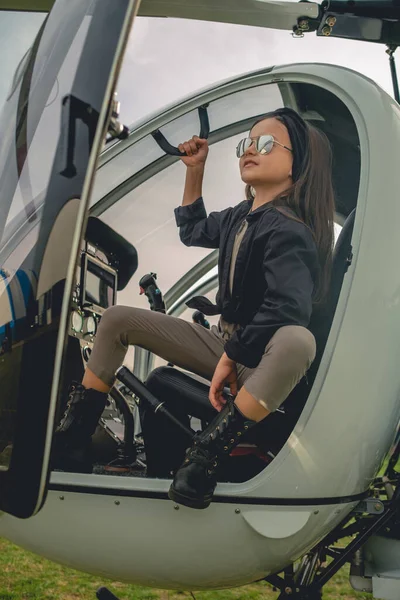 Aynalı güneş gözlüklü gülümseyen genç kız helikopter kokpitinden gökyüzüne bakıyor.