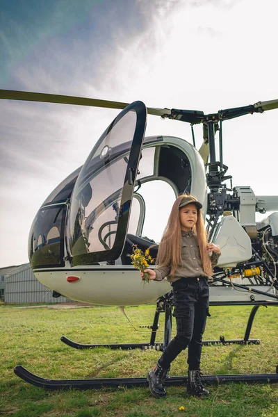 Bir buket kır çiçeğiyle helikopterin yanında duran küçük kız.