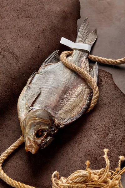 Соленый сушеный таракан с бумажной этикеткой на хвосте и грубой веревкой на кожаном фоне — стоковое фото