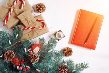 Noel ya da yeni yıl arkaplanı: kürk ağacı, dallar, hediyeler, dekorasyon, beyaz arka planda kırmızı defter. Güneş parlaması