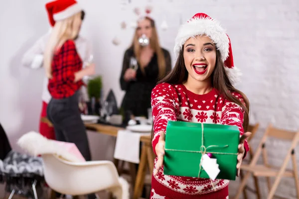 Ritratto di una giovane donna con scatole regalo verdi in primo piano a casa. Bella bruna in un cappello di Babbo Natale, costume rosso con cervi — Foto Stock