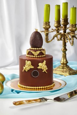 Çikolatalı paskalya pastası, üstünde altın süslemeler ve çikolata yumurtası, Paskalya kutlamaları için lüks bir ortam oluşturuyor.