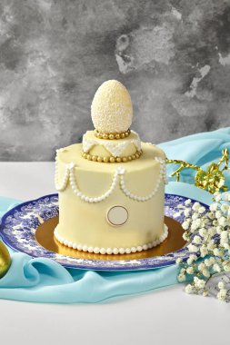 Beyaz hindistan cevizi yumurtası, altın ve beyaz incilerle süslenmiş küçük, zarif bir paskalya pastası.