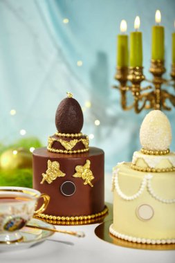 Çikolata yumurtaları, altın melekler ve boncuklarla süslenmiş iki güzel paskalya pastası lüks ve zarif bir festival sahnesi yaratıyor.