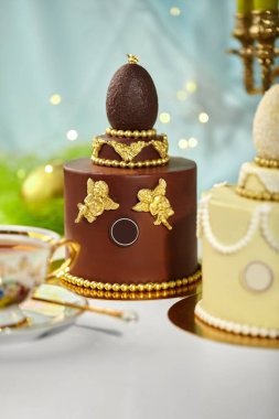 Çikolatalı paskalya pastası. Çikolatalı yumurta, altın melekler ve altın boncuklarla süslenmiş. Bir fincan çayla servis ediliyor.