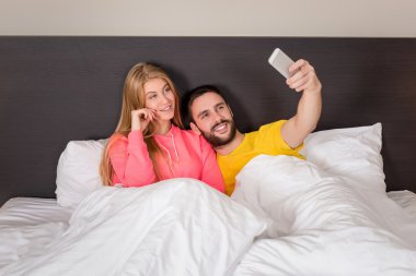 Young happy couple on bed doing selfie with telephone camera.