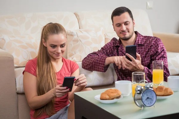 Linda pareja joven desayunando y mirando el teléfono móvil — Foto de Stock