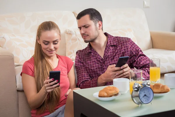 Linda pareja joven desayunando y mirando el teléfono móvil — Foto de Stock