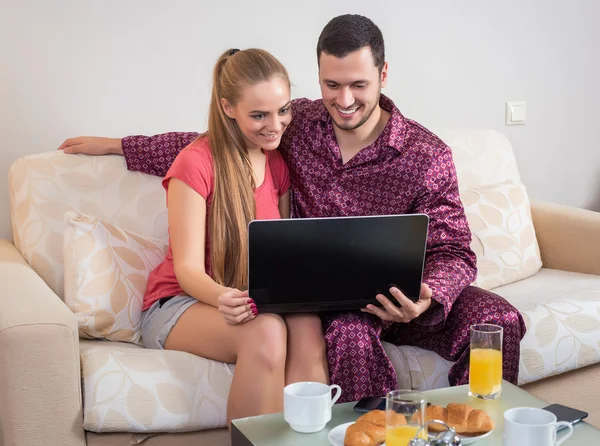 Linda pareja joven desayunando, frente a la computadora portátil — Foto de Stock