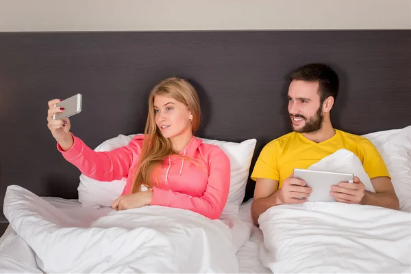 Joven feliz pareja en la cama haciendo selfie con cámara de teléfono . — Foto de Stock