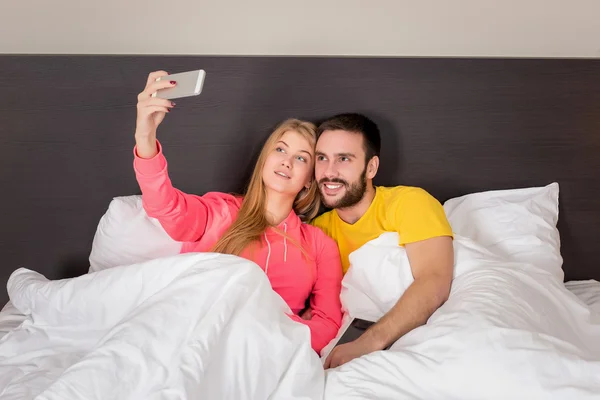 Joven feliz pareja en la cama haciendo selfie con cámara de teléfono . — Foto de Stock