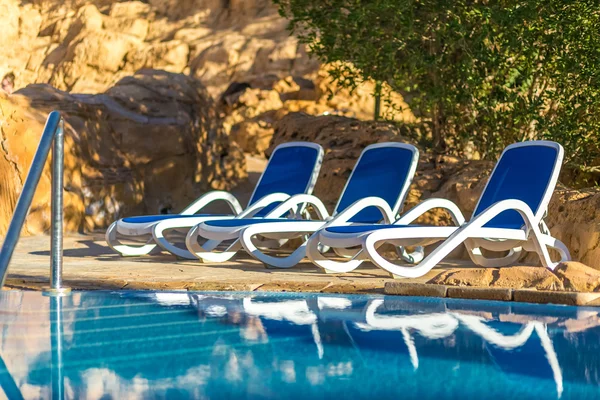 Several of sun loungers by beautiful swimming pool and treess. — Stock fotografie