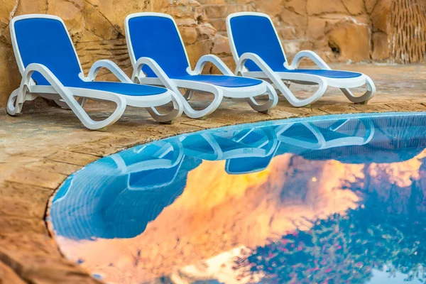 Three sunloungers reflected in blue water of the swimming pool — Stock fotografie