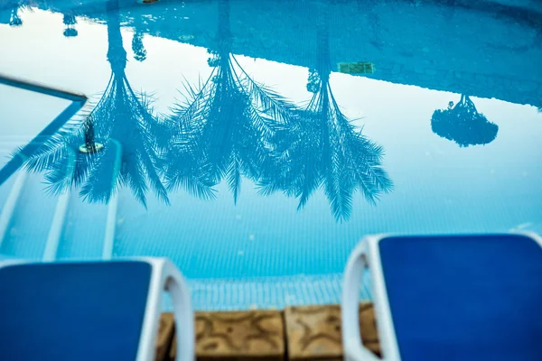Closeup lehátky a bazén s odraženým palmy ve vodě — Stock fotografie