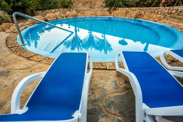 Espreguiçadeiras e piscina com palmeiras refletidas na água — Fotografia de Stock