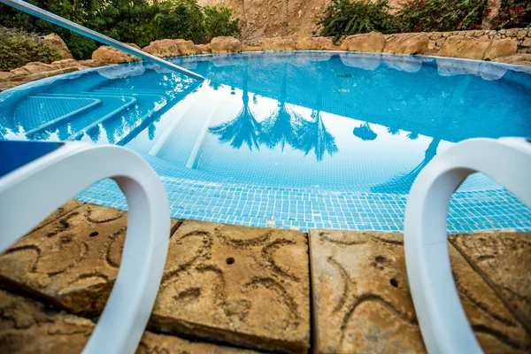 Encerrar espreguiçadeiras e piscina com palmas refletidas na água — Fotografia de Stock