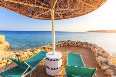 Umbrellas and two empty deckchairs on the shore sand beach