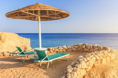 Umbrellas and two empty deckchairs on the shore sand beach