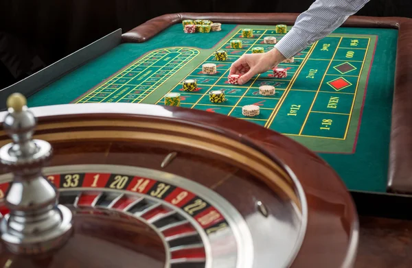 Ruleta y montones de fichas de juego en una mesa verde . — Foto de Stock