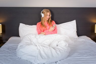 Genç kadın yatakta smartphone üzerinden müzik dinleme