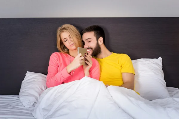 Молодая сладкая пара в постели Смотря что-то на планшетном гаджете — стоковое фото