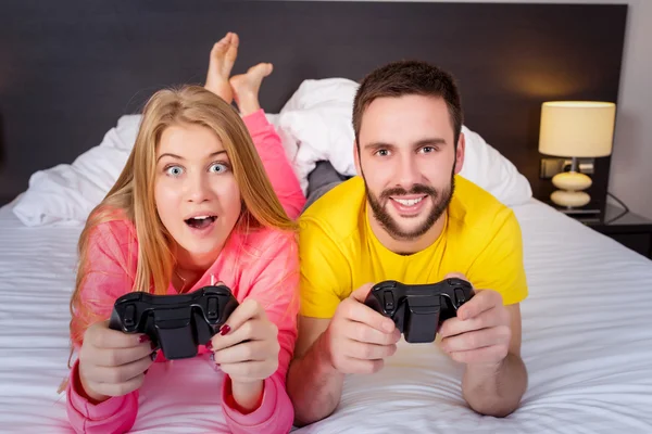 Lyckliga unga paret ha kul spela videospel i sängen — Stockfoto