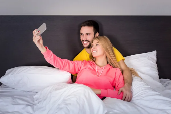 Молодая счастливая пара на кровати делает селфи с телефоном . — стоковое фото