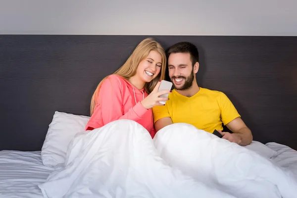 Joven pareja dulce en la cama mirando un teléfono móvil — Foto de Stock