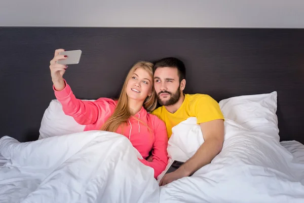 Joven feliz pareja en la cama haciendo selfie con cámara de teléfono . — Foto de Stock