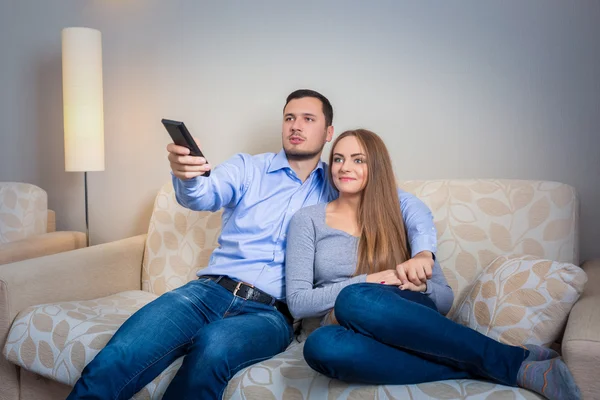 Happy couple sitting on sofa watching television together — Stock Fotó