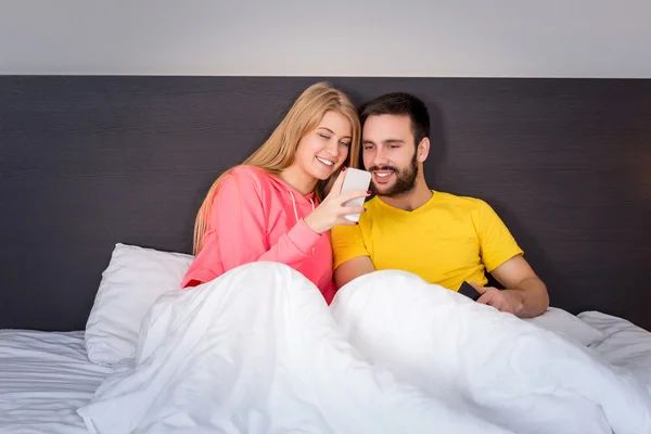 Joven pareja dulce en la cama mirando un teléfono móvil — Foto de Stock