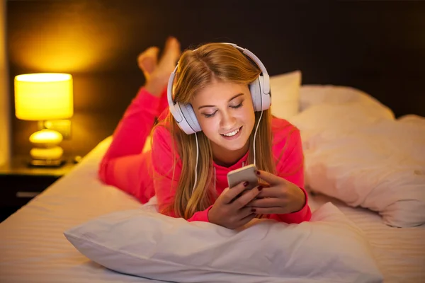 Νεαρές γυναίκες που ακούτε τη μουσική από το smartphone στο κρεβάτι — Φωτογραφία Αρχείου