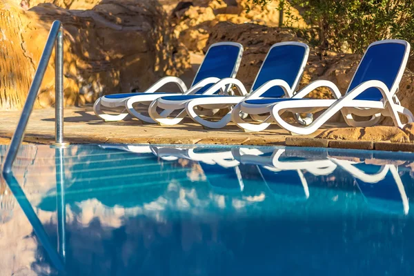 Sunloungers poblíž bazén a odráží jejich v modré vodě — Stock fotografie