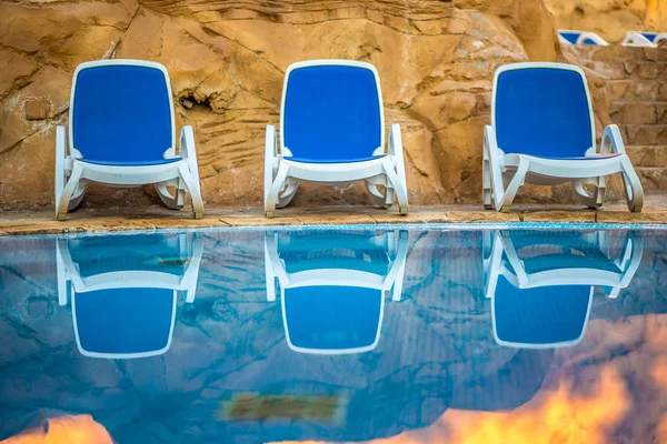 Sunloungers poblíž bazén a odráží jejich v modré vodě — Stock fotografie