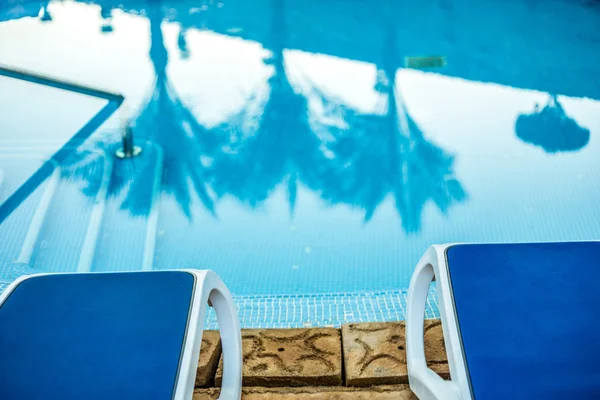 Closeup lehátky a bazén s odraženým palmy ve vodě — Stock fotografie
