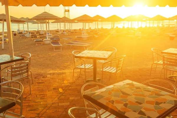 Praia com espreguiçadeiras, guarda-sol e bar durante o nascer do sol — Fotografia de Stock