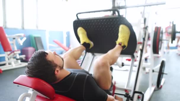 Atractivo joven haciendo la prensa de la pierna en la máquina en el gimnasio — Vídeos de Stock