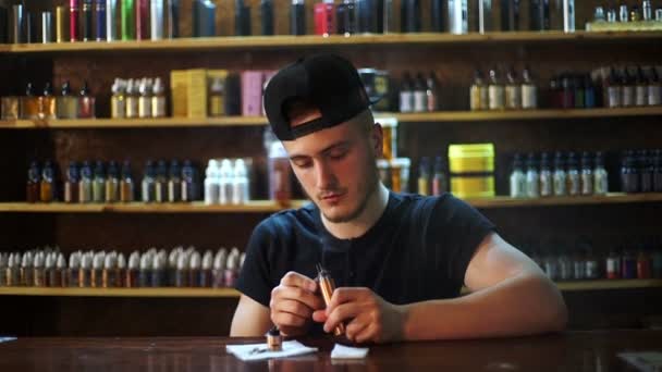Junger Verkäufer im Vape-Shop installiert Baumwolle im Zerstäuber-Schaufenster im Hintergrund — Stockvideo
