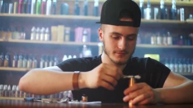 vape dükkanda genç satıcı pamuk atomizer gösterisi penceresinde arka planda yükleme