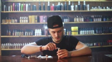 vape dükkanda genç satıcı pamuk atomizer gösterisi penceresinde arka planda yükleme