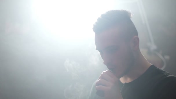 Jovem homem vaper exalando grandes nuvens de fumaça com vape e-cigarro em câmara lenta — Vídeo de Stock